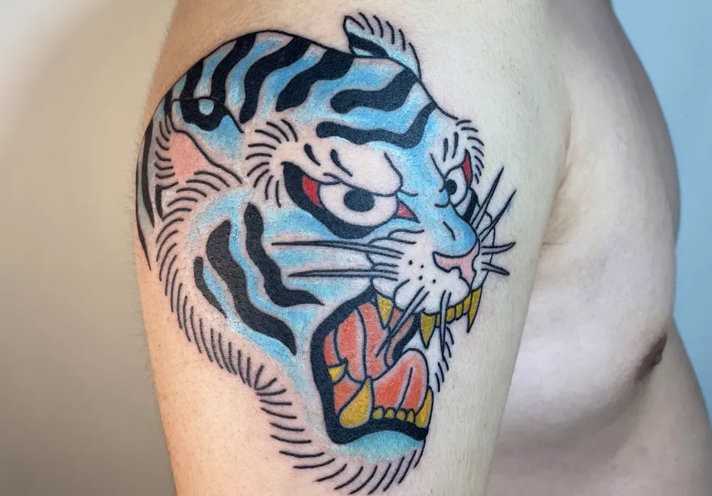 Blue tiger head tattoo in American Traditional style on the upper arm