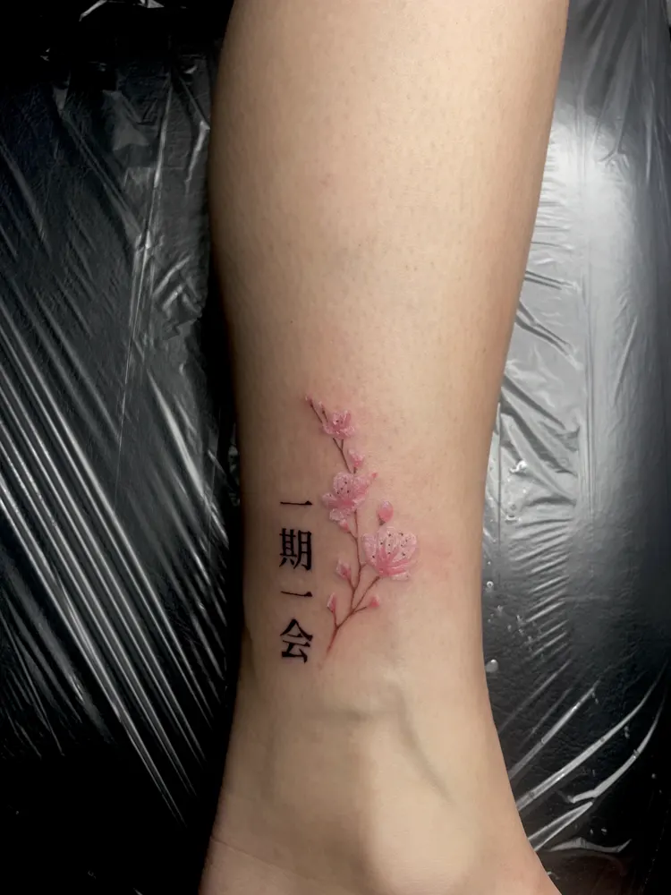 Pink cherry blossom tattoo with the kanji ichigo ichie on the ankle