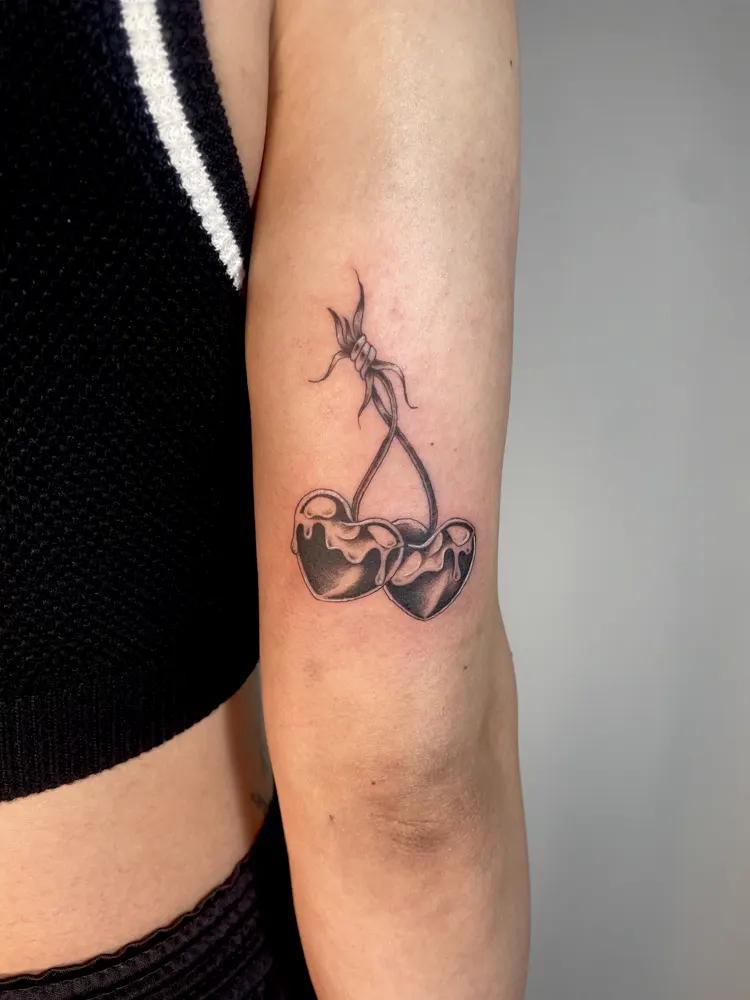 Black and grey heart-shaped cherries tattoo on the back of the upper arm