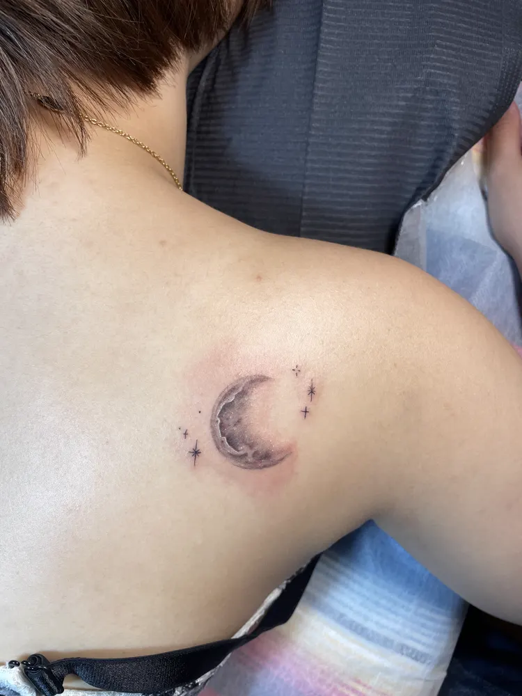 Small crescent moon and stars tattoo in soft black and grey on the shoulder blade