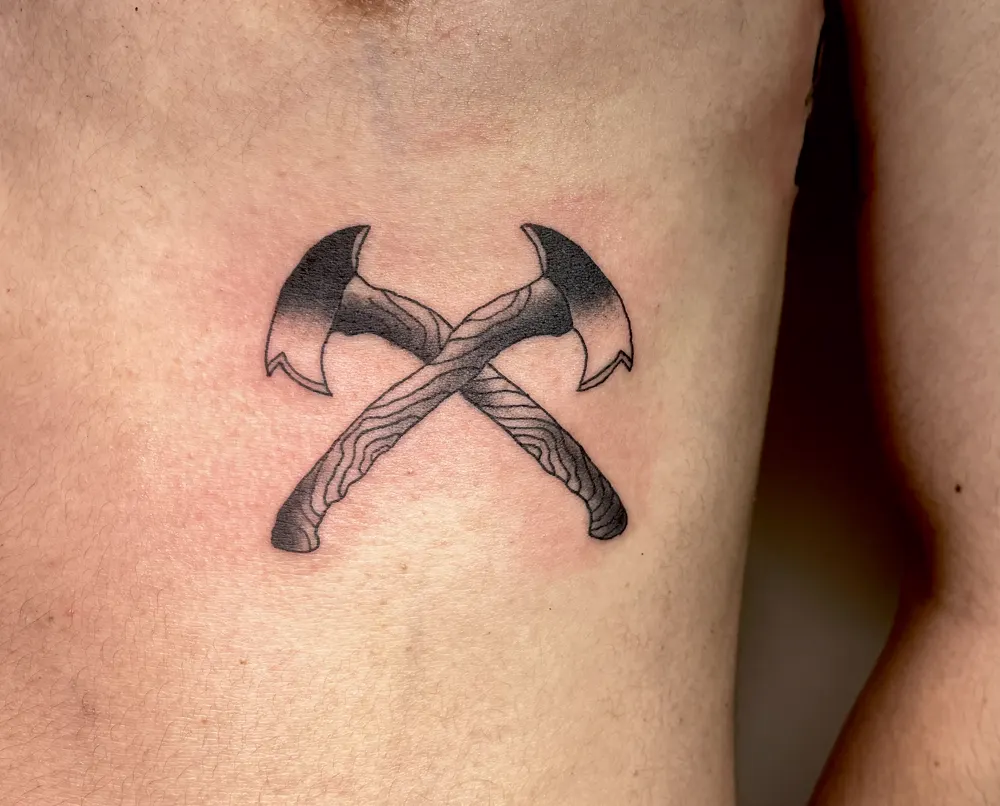 Black and grey crossed axes tattoo on the ribs