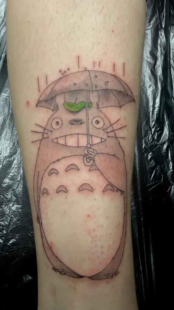 Forest spirit tattoo holding an umbrella with a green leaf on the shin