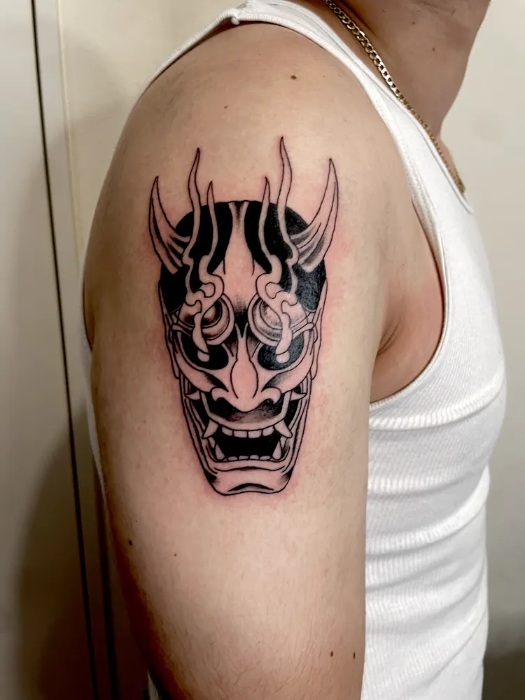 Black and grey Hannya mask tattoo with curling horns on the upper arm