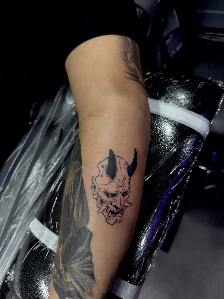 Black Hannya mask tattoo with solid black horns on the forearm