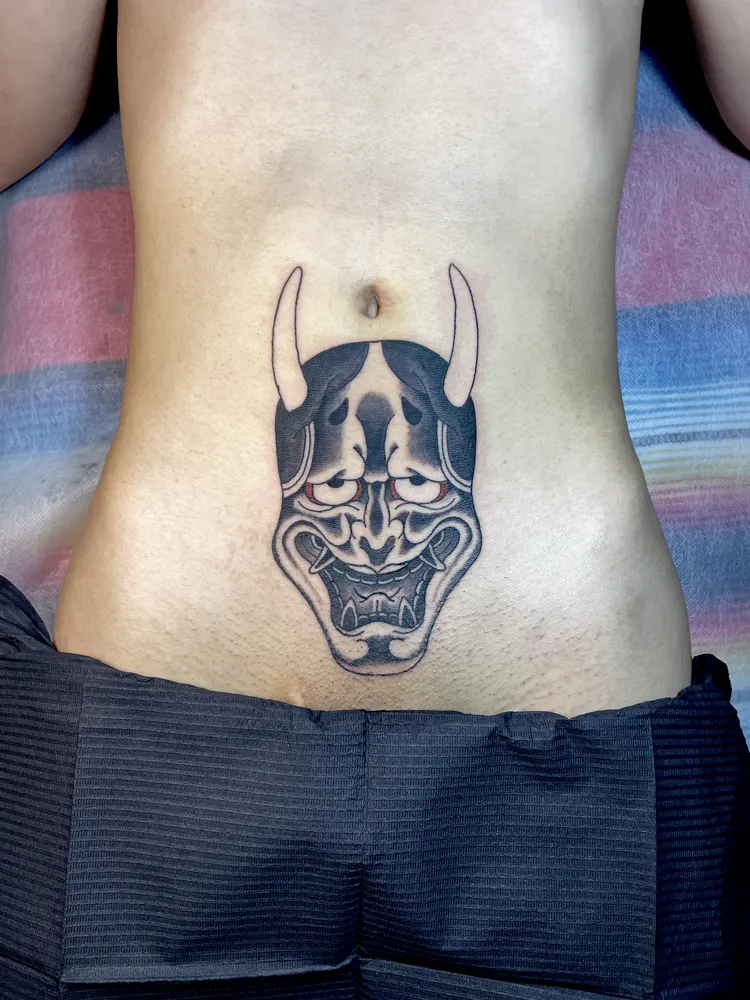 Black and grey Hannya mask tattoo with red eyes on the stomach