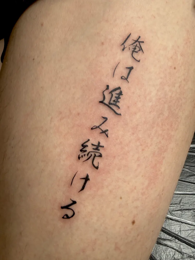 Vertical Japanese calligraphy tattoo in black ink on the thigh