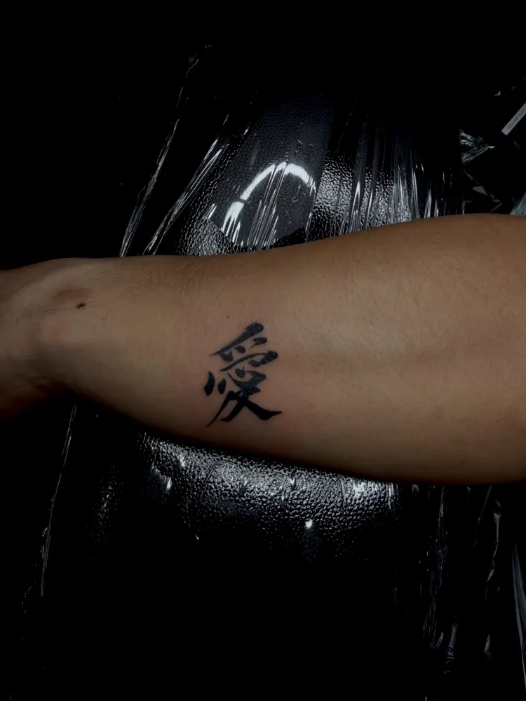 Kanji for love tattoo in bold brush strokes on the forearm