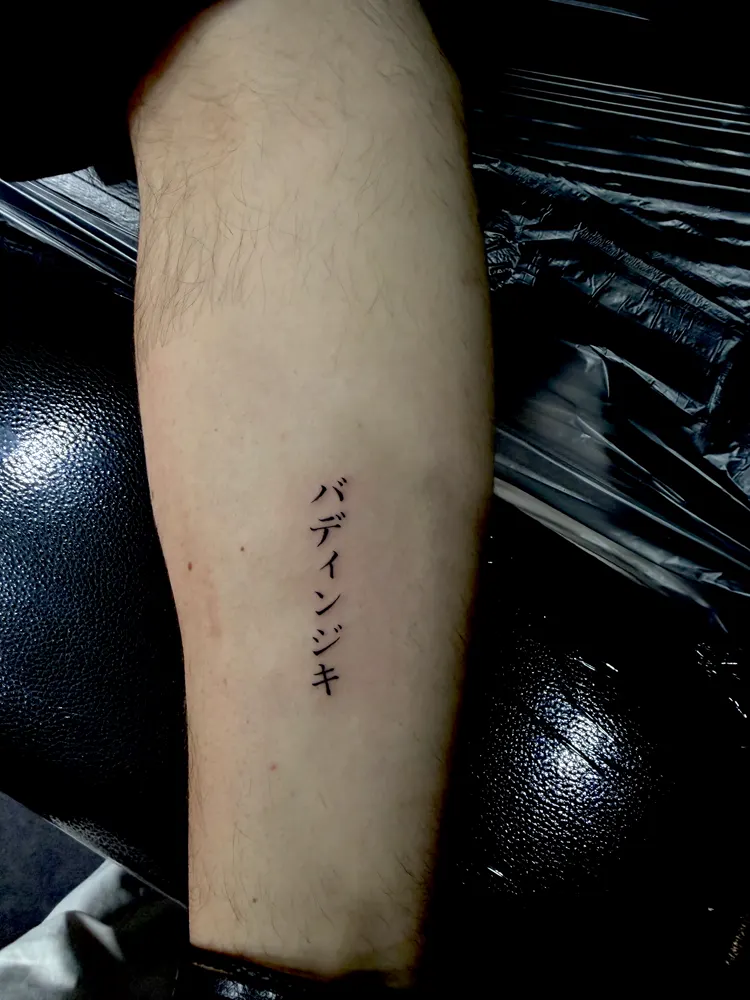 Vertical katakana lettering tattoo in black on the shin