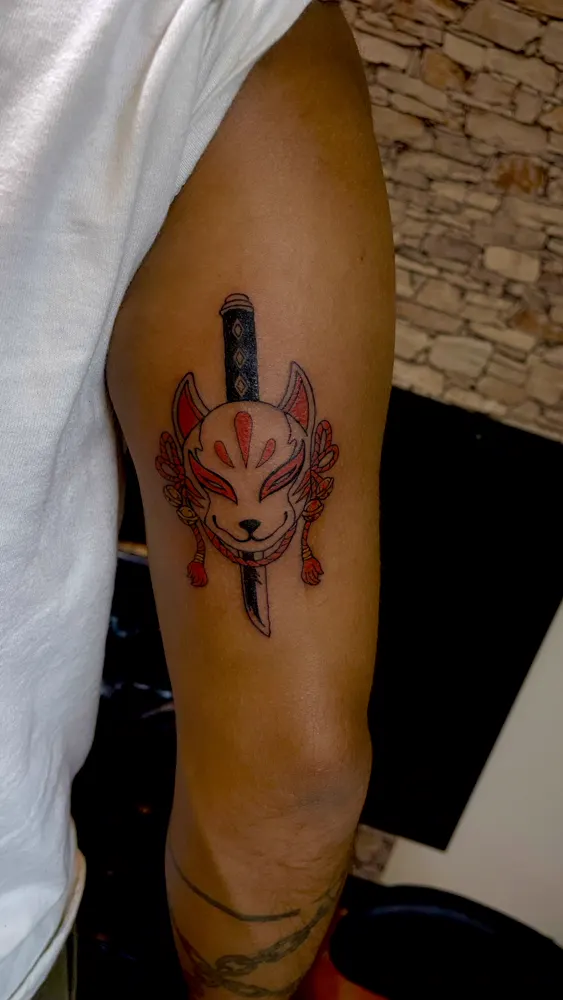 Red and black kitsune mask and tanto tattoo on the upper arm