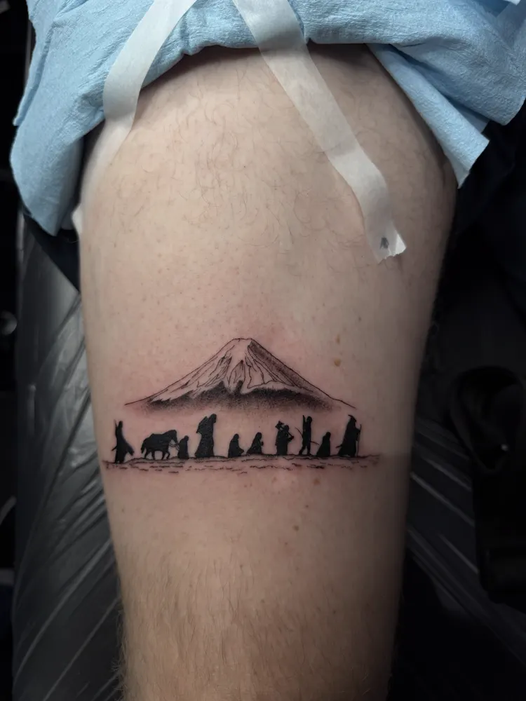 Mountain and travelers silhouette tattoo in black and grey on the thigh
