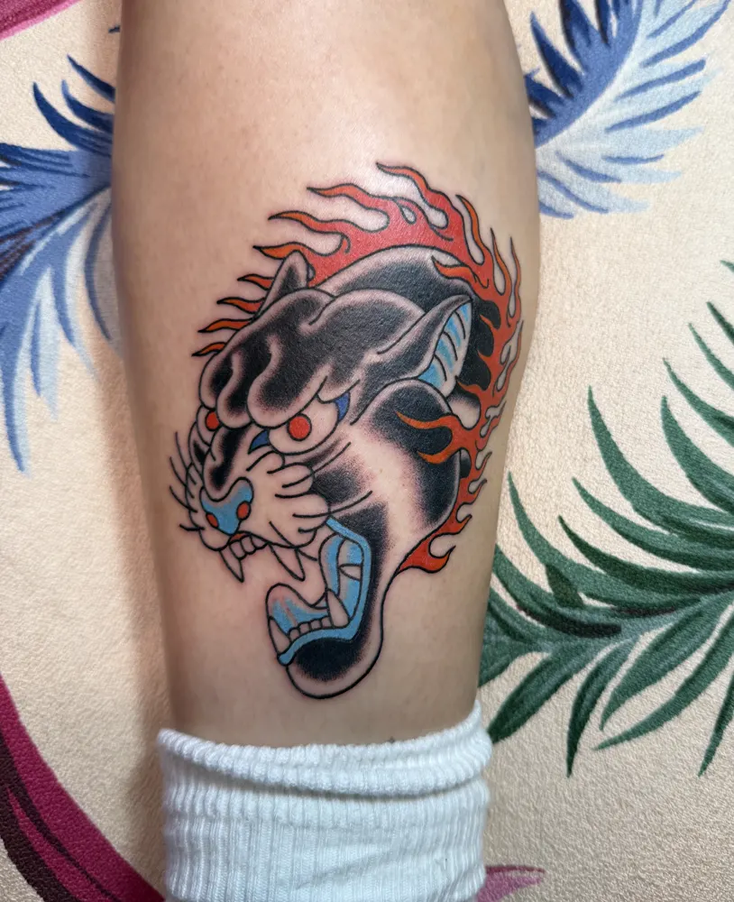 Black panther head tattoo with red flames and a blue mouth on the calf