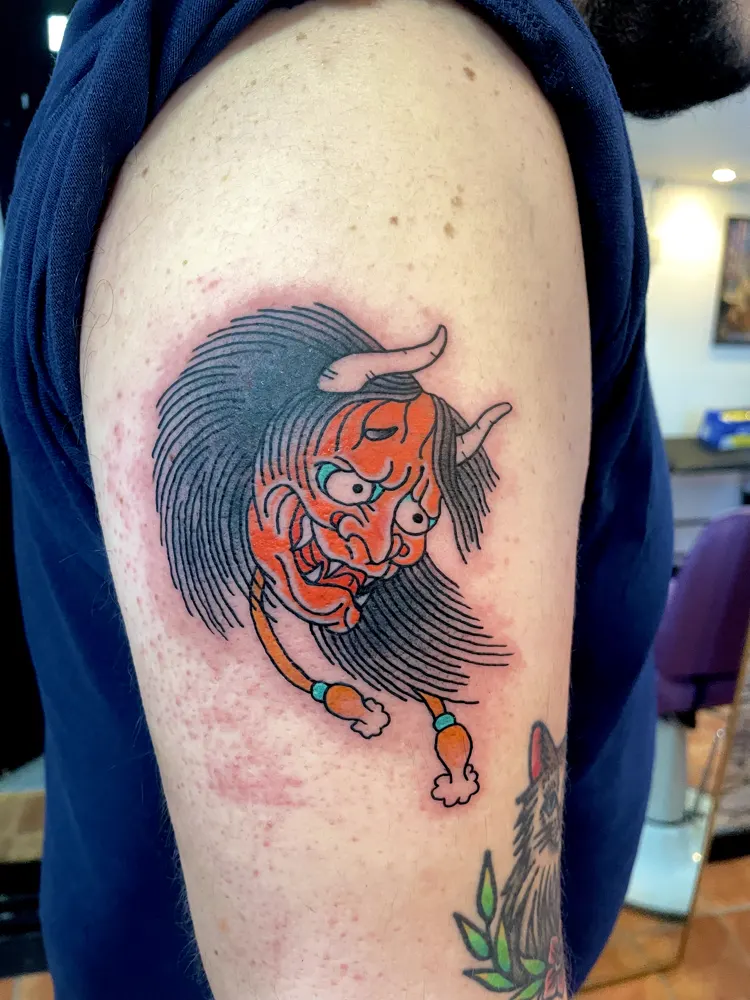 Red oni tattoo with horns and long black hair on the upper arm