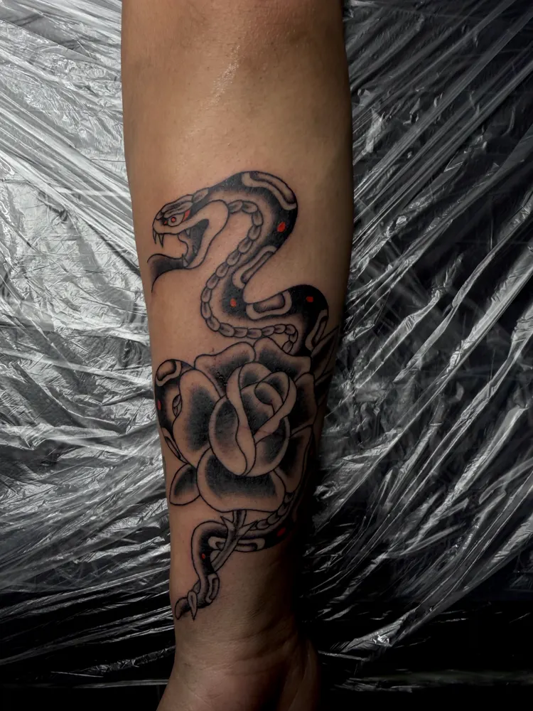 Black and grey snake and rose tattoo with red accents on the forearm