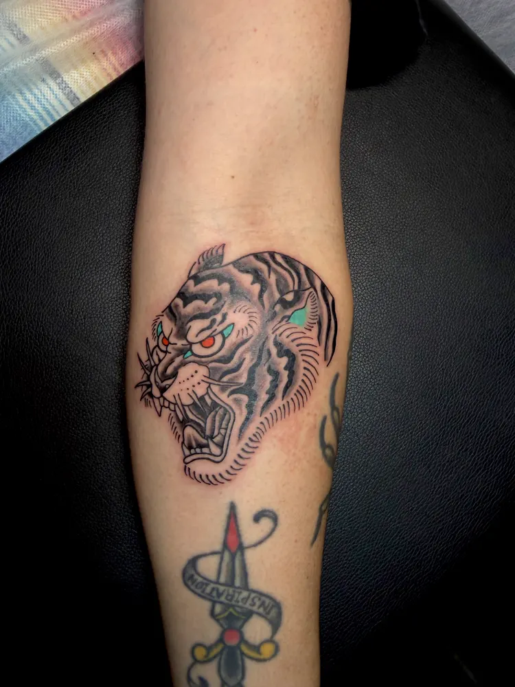 Tiger head tattoo in black and grey with red eyes on the forearm