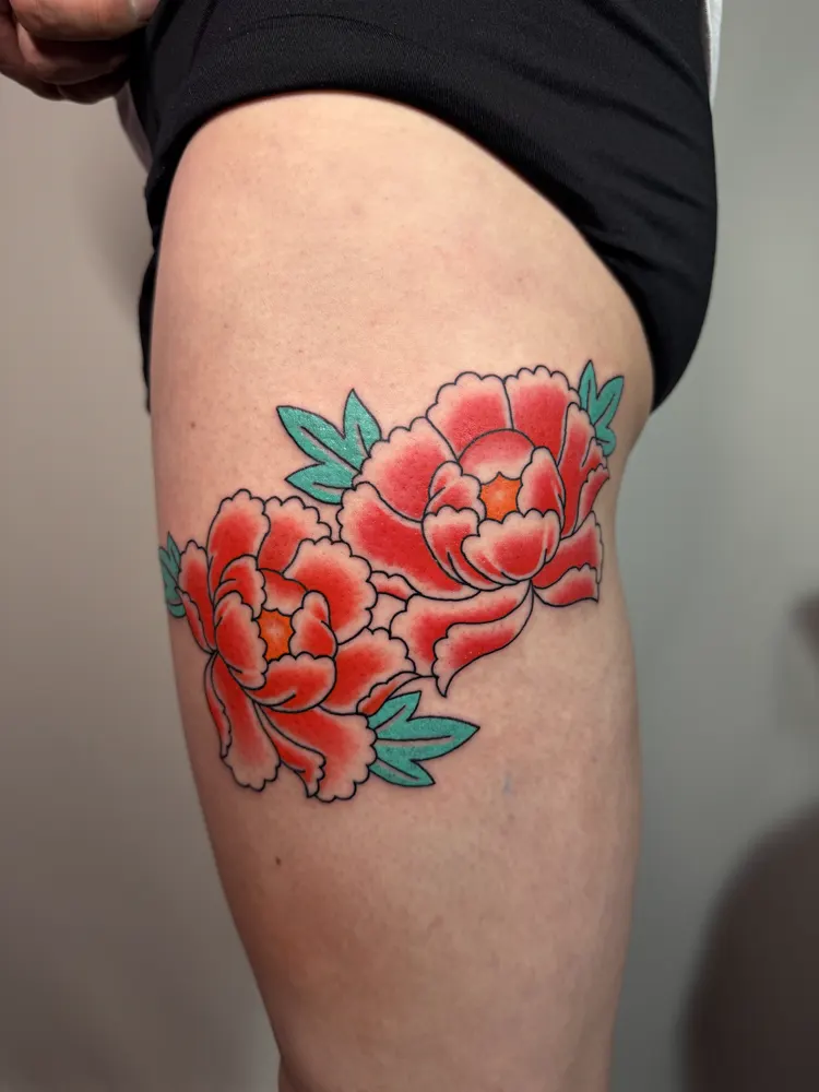 Two red Japanese peonies tattoo with green leaves on the thigh